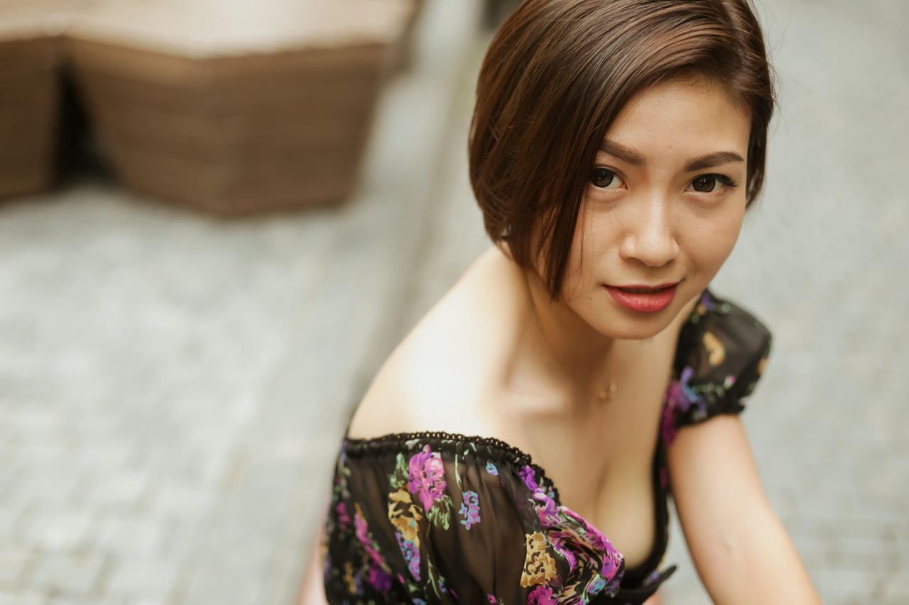 A portrait of a woman in a floral dress sitting outdoors with a soft focus background.